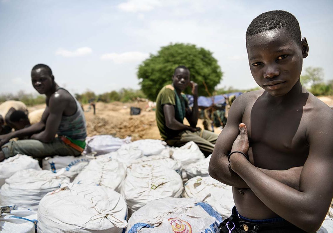 A child sits on bags full of stones that will be sent to the village to extract the gold.