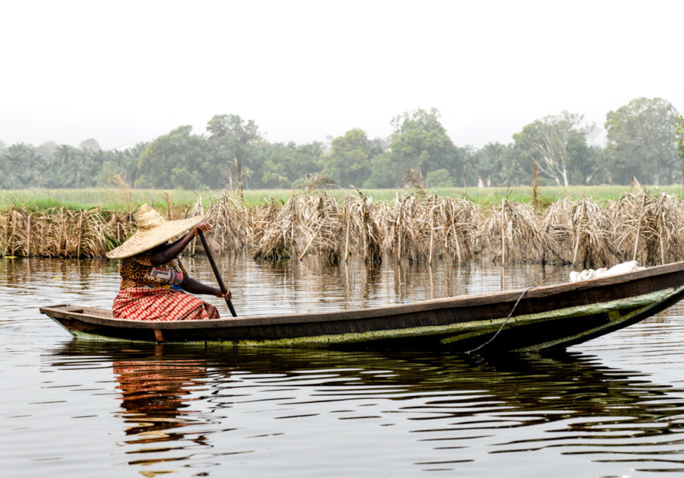 Ganvié Africa, West Africa, Benin, Lake Nokoue, Ganvié. Woman rowing in the back of a pirogue outside the lakeside town of Ganvié on Lake Nokoue.