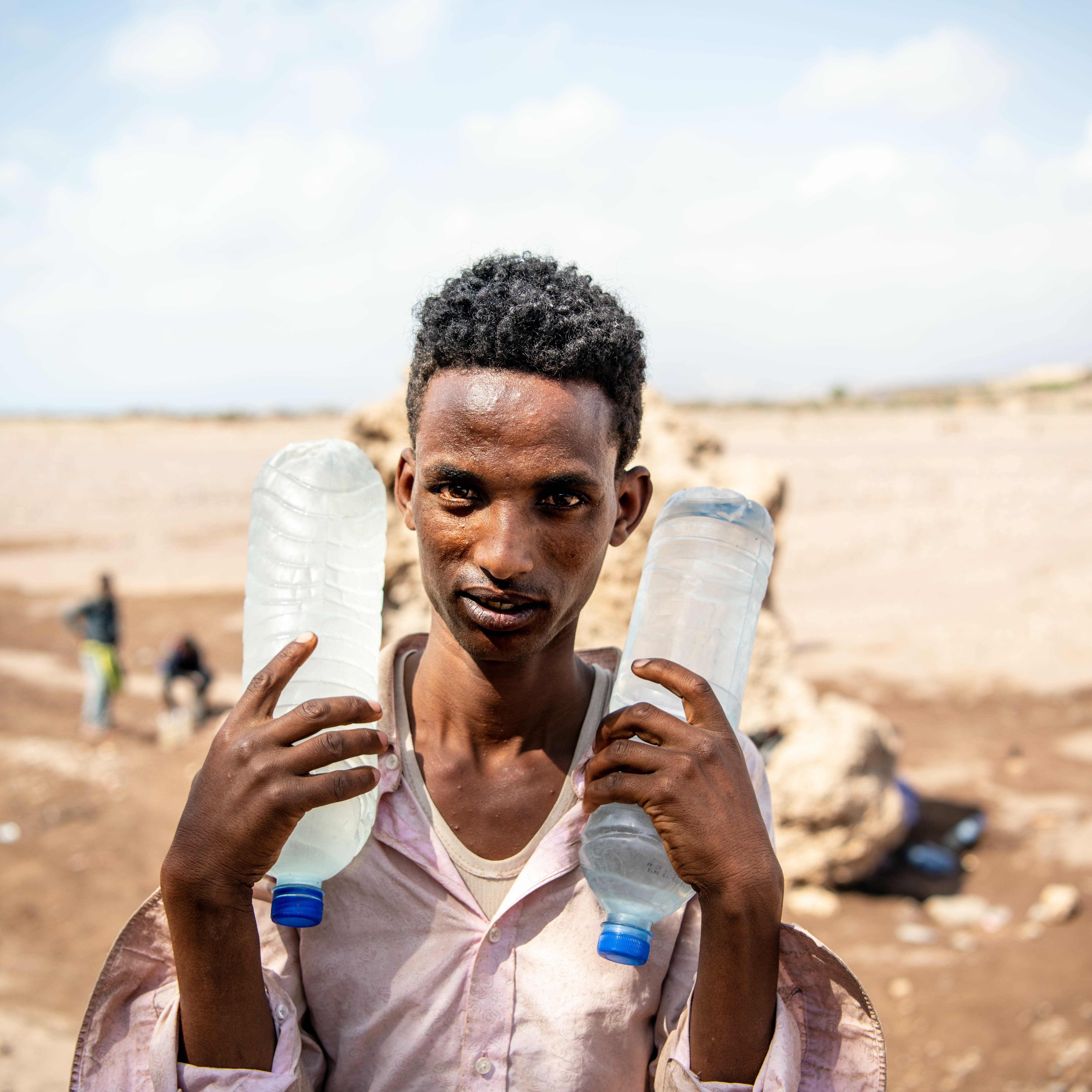 Portrait of a migrant in Alat Ela carrying water bottles he filled up from a hole in the ground down the hill